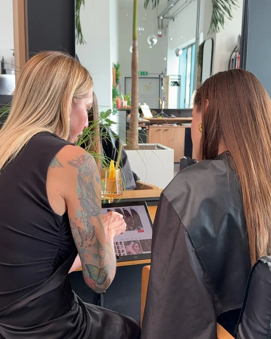 Friseurmeisterin Jasmin Werner im Beratungsgespräch mit einer Kundin, gemeinsam sehen sie sich Frisurenbilder auf einem Tablet an