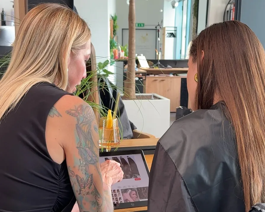 Friseurmeisterin Jasmin Werner im Beratungsgespräch mit einer Kundin im Salon QUERSCHNITT in Baden: Gemeinsam sehen sie sich Frisurenbilder auf einem Tablet an