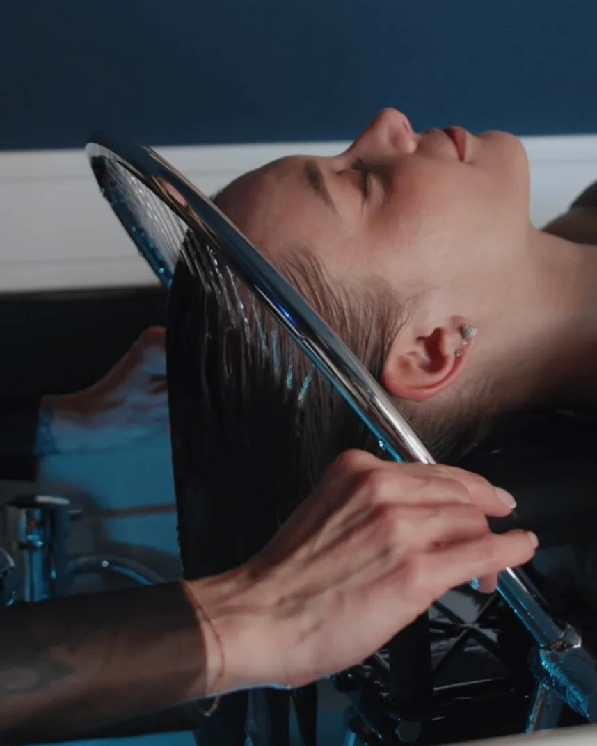 Head-Spa-Ritual bei QUERSCHNITT: Ein Model entspannt mit geschlossenen Augen unter der Regendusche am Head-Spa-Becken, Friseurmeisterin Jasmin Werner führt das Wasser