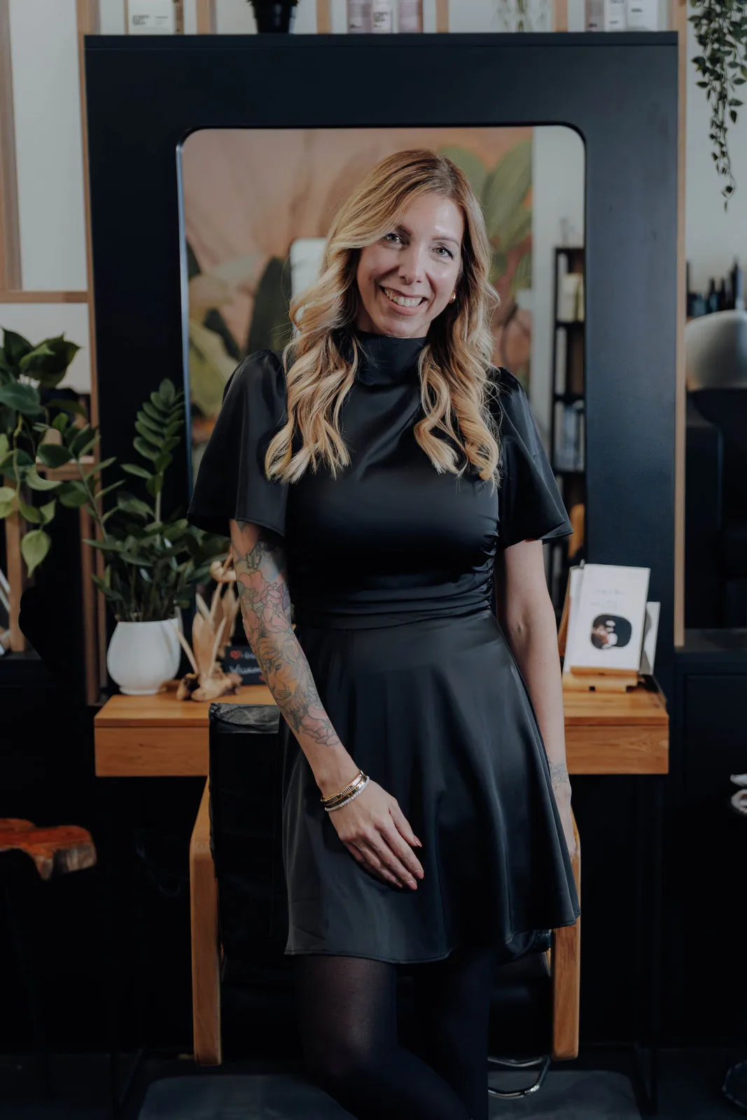 Jasmin Werner, Friseurmeisterin, lächelnd im schwarzen Kleid vor einem Spiegelplatz in ihrem Salon in Baden