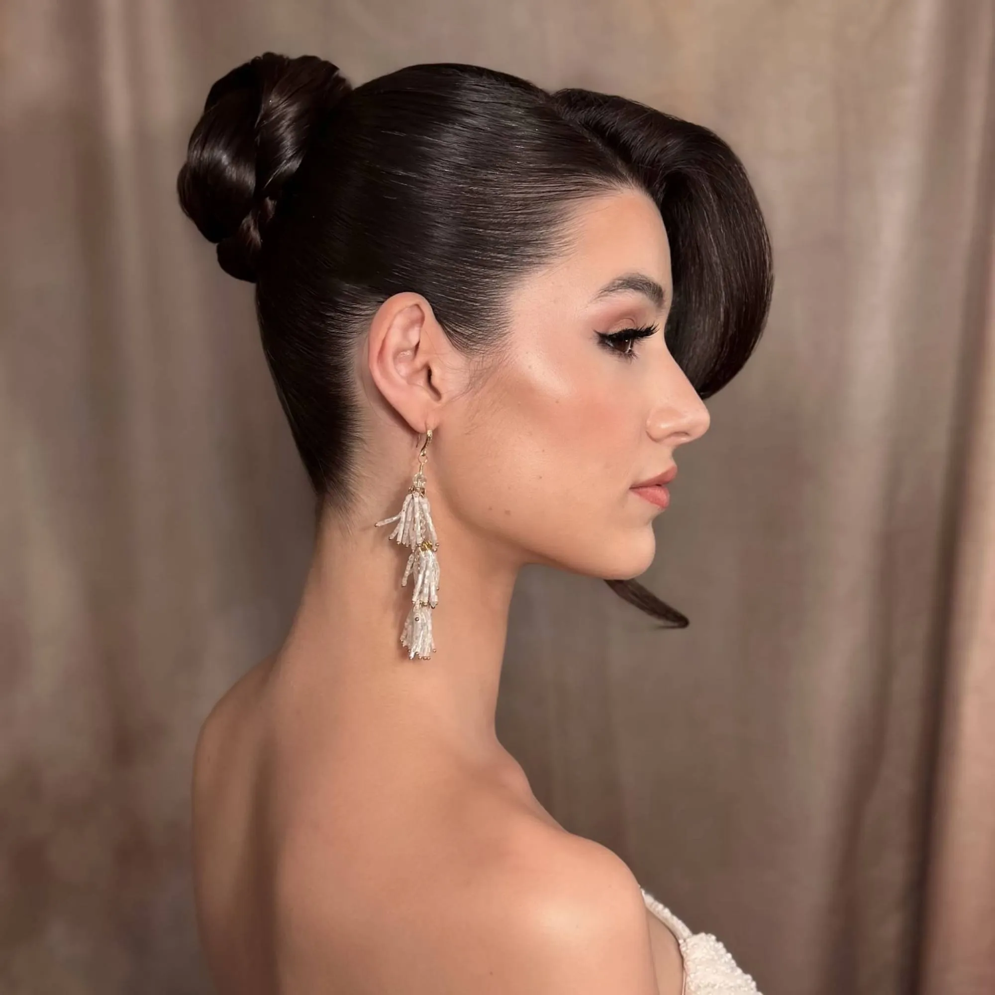 Bridal Hair von Kasia Fortuna: dunkler, glatt gestylter hoher Dutt mit voluminöser, seitlich geschwungener Partie über der Stirn, im Profil