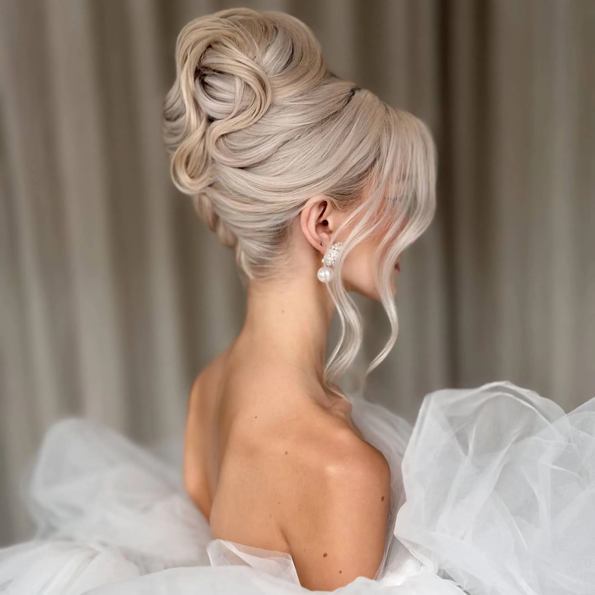 Bridal Hair von Kasia Fortuna: hohe, voluminöse Hochsteckfrisur in hellem Blond mit modellierten Wellen und Pearl-Ohrringen