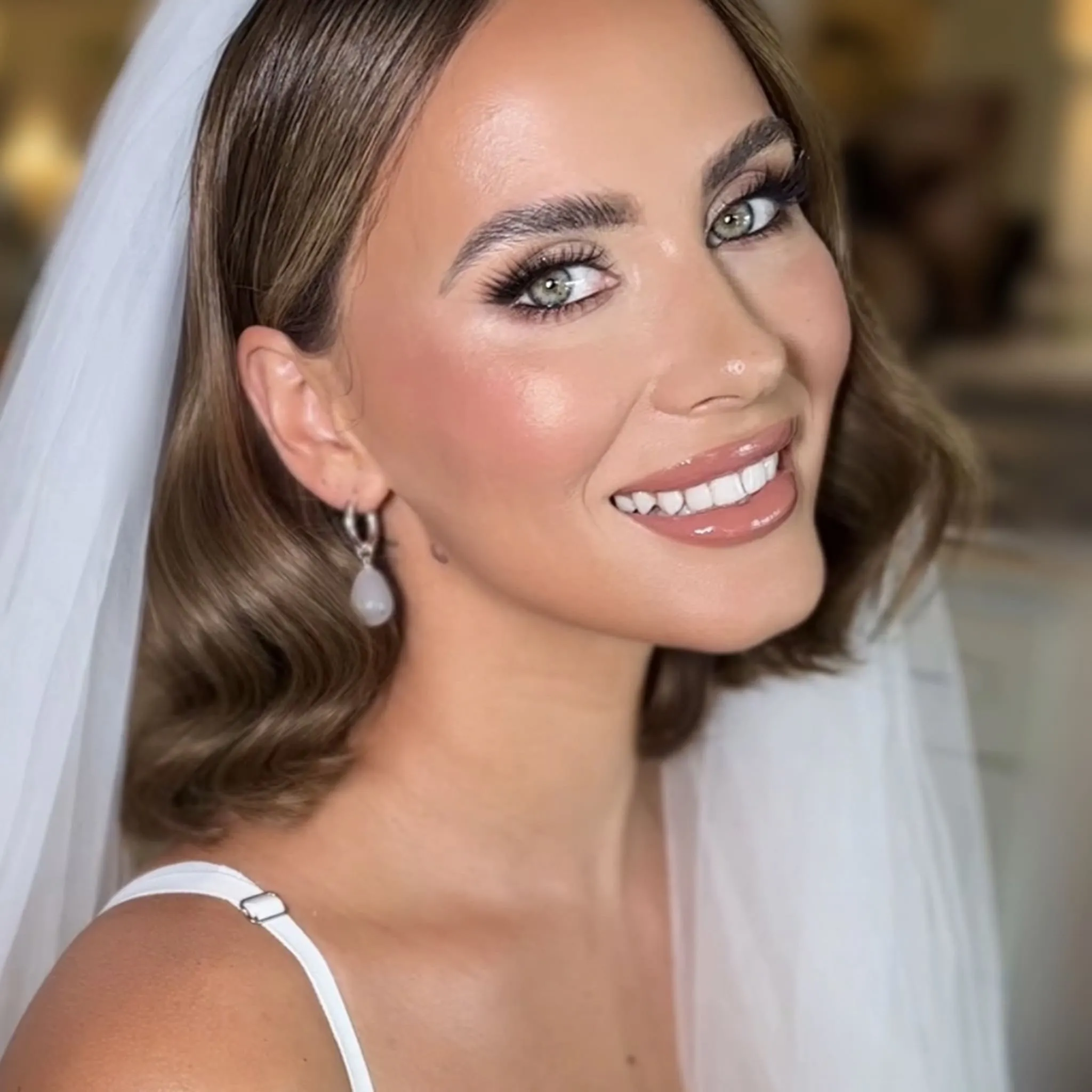 Bridal Make-up von Kristina Gasperas: lächelnde Braut mit Schleier, warmes Augen-Make-up und gewellter Bob