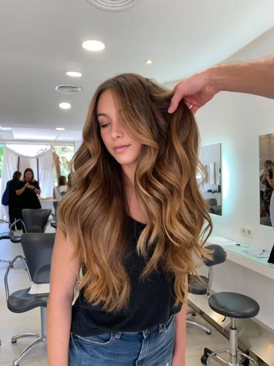 Brünettes Haar mit warmem Karamell-Balayage und großen Wellen im Salon